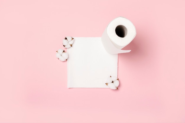 Roll of paper towels and cotton flowers on a pink surface. Concept is 100 natural product, delicate and soft. Flat lay, top view