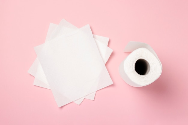 Roll of paper towels and few pieces towels on a pink background. Concept is 100% natural product, delicate and soft. Flat lay, top view. Banner