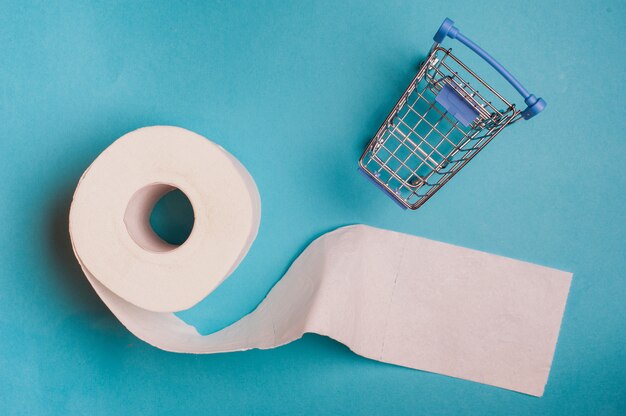 Roll of toilet paper and little shopping cart on blue background.