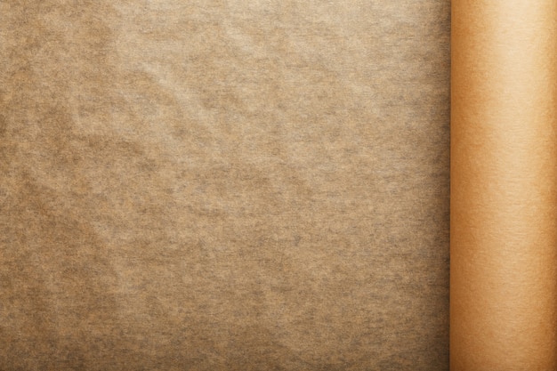 A roll of unfolded brown parchment paper, for baking food in on a dark background, top view.