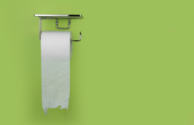 Roll of white toilet paper on a background of green wall copy space. Shortage of toilet paper.