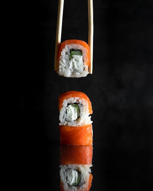 Roll with salmon in chopsticks isolated on black