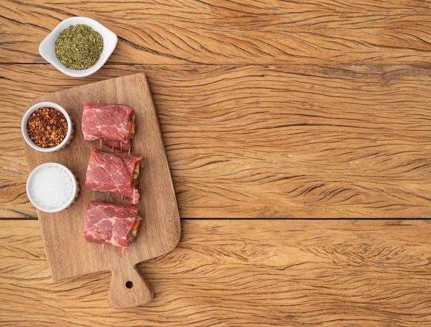 Foto carne di manzo arrotolata o involtino di verdure e pancetta ripiena di carne su un tavolo di legno con condimenti e spazio per la copia