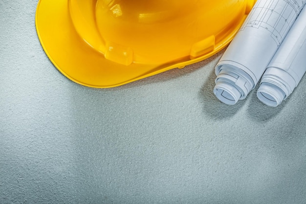 Rolled blueprints hard hat on concrete background.