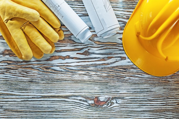 Rolled construction plans building helmet safety gloves on vintage wooden board