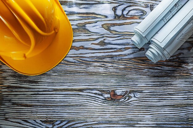 Rolled construction plans hard hat on vintage wooden board.