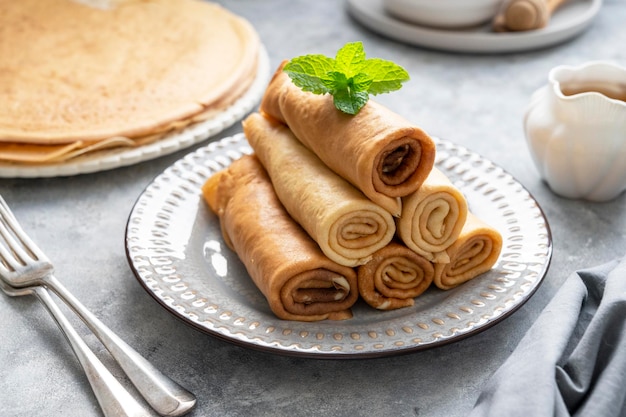 Rolled crepes or thin pancakes, served with jam and honey, on grey background.