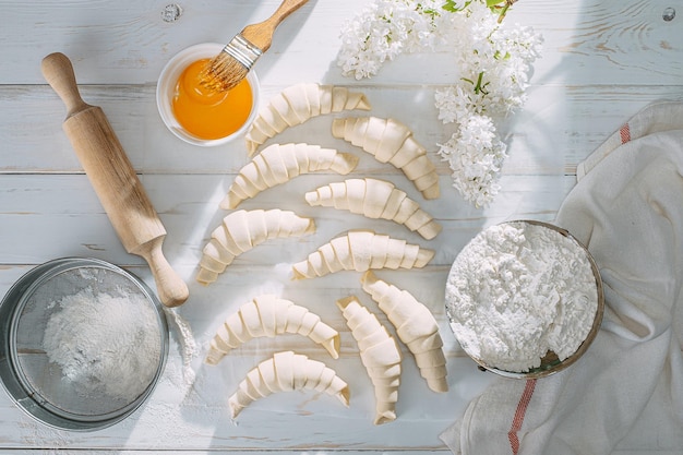 Rolled croissant dough and ready for baking on a white wooden table on baking paper in the morning sun