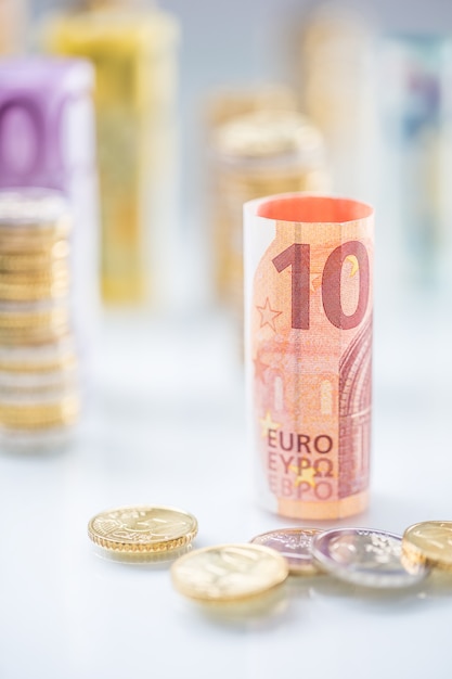 Foto banconote in euro arrotolate e torri di monete impilate in altre posizioni.