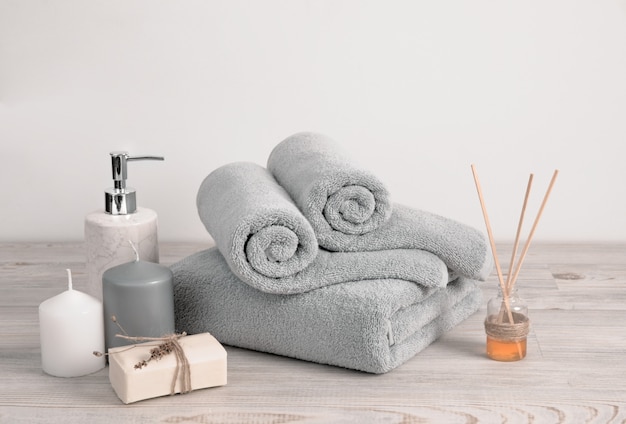 Rolled and folded gray terry towels with soap and candles against white wall