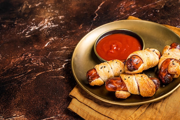 Rolled hot dog sausages baked in puff pastry with ketchup Dark background Top view Copy space