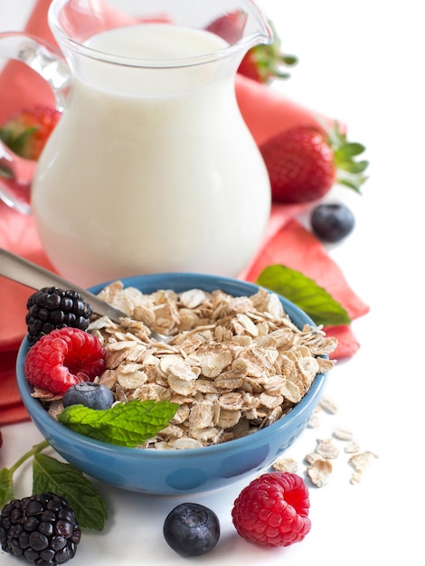 Avena rotolata in una ciotola con frutti di bosco e latte isolato su bianco