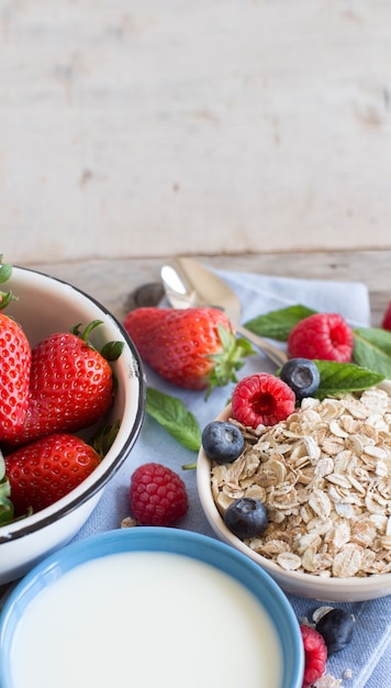 Rolled oats in a bowl with berries  and milk on wood