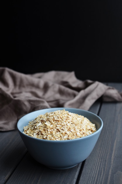 Rolled oats in ceramic bowl on dark wood