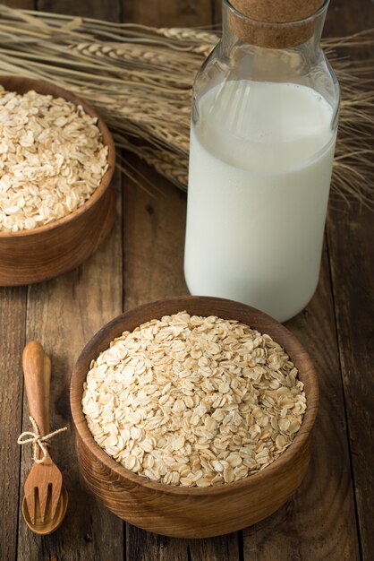 Rolled oats, oats in bowl and jug of milk on wood