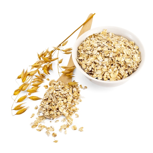 Rolled oats in a wooden spoon and a white porcelain bowl, oat stalks isolated on white background