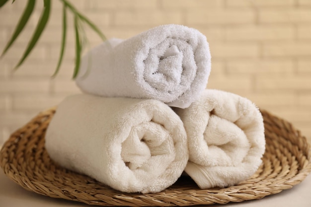 rolled terry towels and green leaves on white table near brick wall indoors closeup