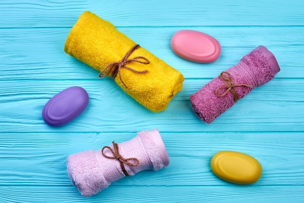 Rolled towels and soap pieces on blue wooden desk. Top view flat lay.