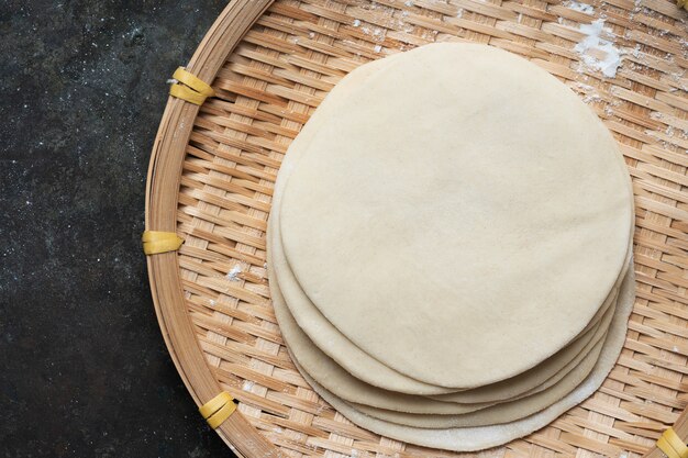 Раскатанное сырое тесто для индийских лепешек чапати на бамбуковом подносе. Готовы приготовить концепцию. Легкое питание. Домашняя еда. Плоский вид сверху