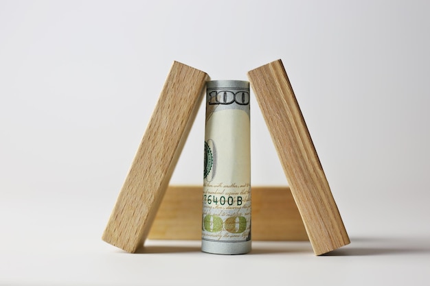 明るい背景に木製の立方体で覆われた 100 ドル札を丸めた。通貨の概念