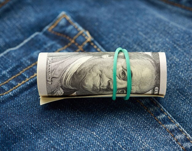 Свернутые долларовые купюры поверх джинсовой ткани