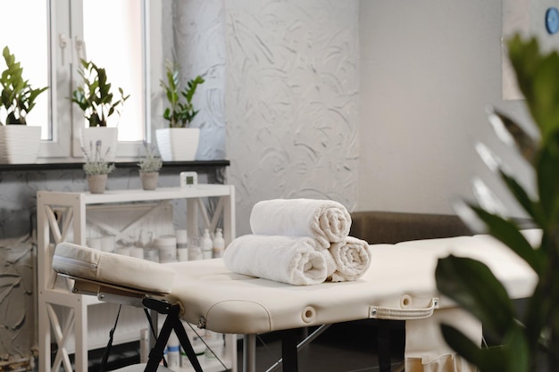Rolled white towels on massage table in empty salon interior of aesthetic clinic nobody modern
