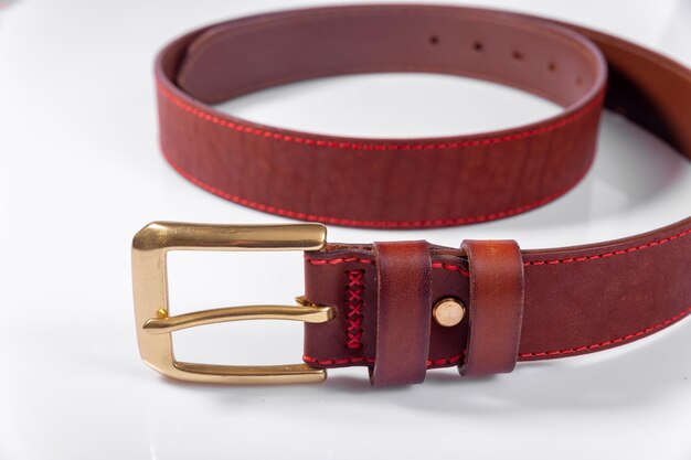 A rolledup brown leather belt with a metal buckle on a white\
background is isolated