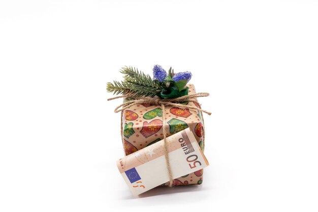 A rolledup paper bill of 50 euros lies with a gift box decorated with a fir branch White background