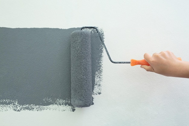 롤러 브러시 페인팅 작업자가 표면 벽에 그림을 그리는 회색 색상 페인트로 아파트 개조 작업 옆에 설명 텍스트를 작성하려면 빈 복사본 공간을 흰색으로 둡니다.