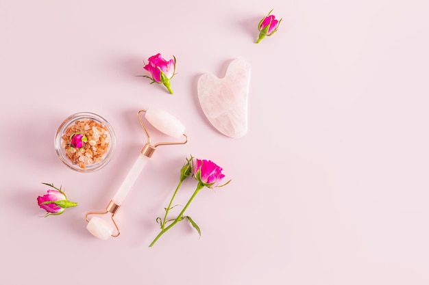 Roller massager for face neck and decalte area Gua sha scraper on a pink background with small rosebuds A copy of the space The concept of beauty