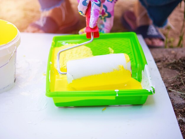 Roller paint tray girl\'s hand rolls out a roller in a tray with\
yellow paint