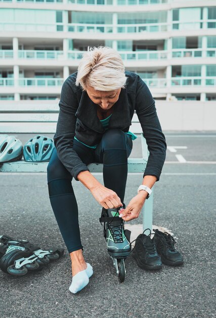 Roller skate tie and senior woman in city ready for sports adventure and fitness hobby outdoors Exercise holiday and elderly female tying shoelace from skating travel and journey in road