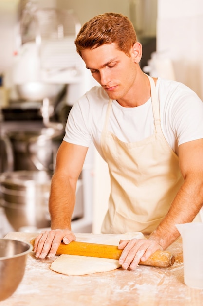 Rolling out the dough. Confident baker rolling out the dough with rolling pin