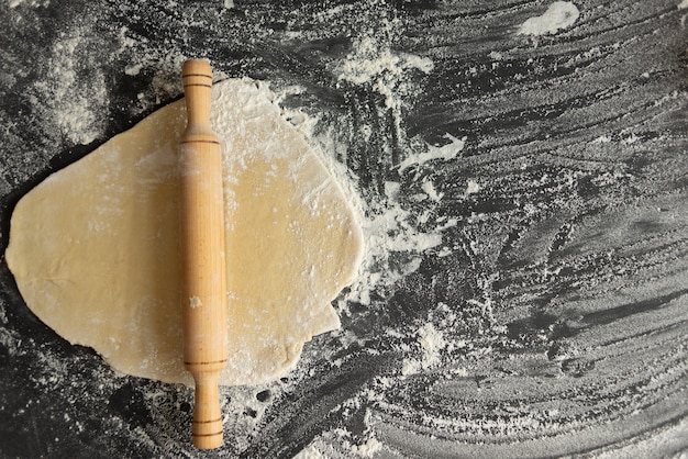 Photo rolling pin on a piece of raw dough, the process of making the cake cake. cook at home