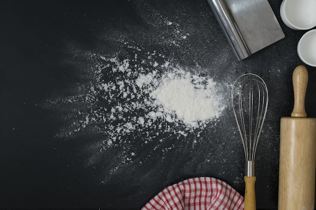 Rolling pin and whisk on the black table spread of flour