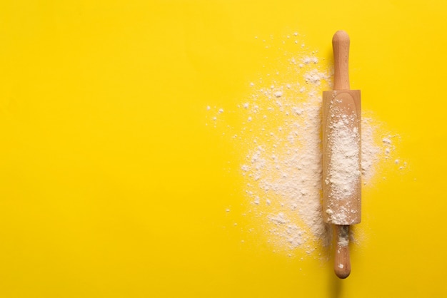 Rolling pin with flour on yellow background. Baking, menu, recipe concept.