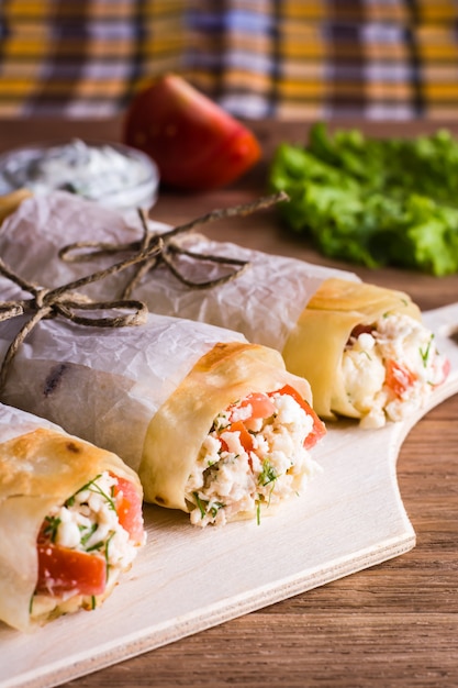 Foto rotoli di pita ripieni di formaggio, pollo e pomodoro e verdure fresche su un tavolo di legno