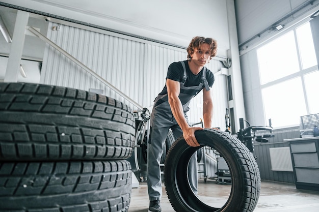 タイヤを転がす灰色の制服を着た大人の男が自動車サロンで働く