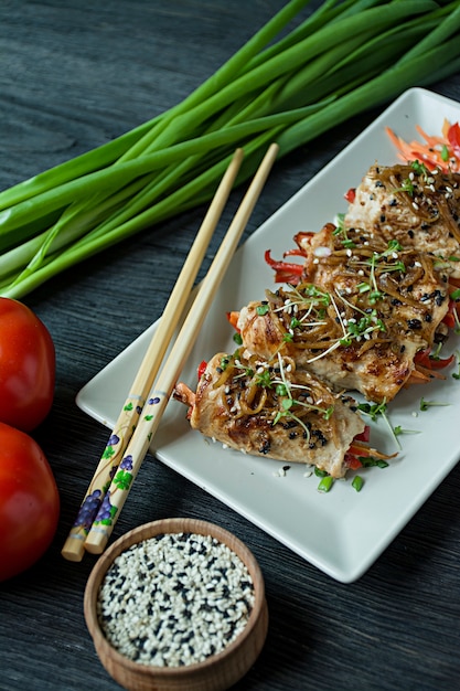 Rolls with fresh chicken breast with greens, carrot slices, bell peppers on a dark cutting board. 