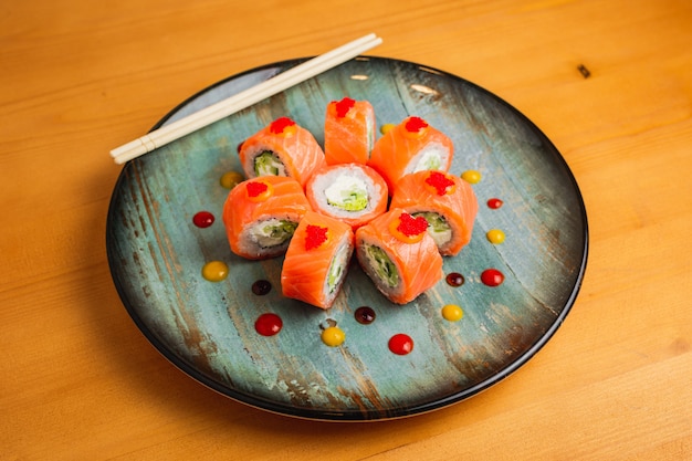 Rolls with salmon decorated with flying fish caviar on a blue plate