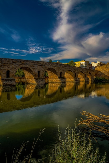 Roman bridge of Merida symmetrically reflects the bridge in the dark water Cloudy twilight sky
