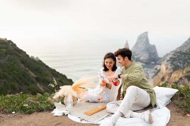 Romance by the sea happy couple having picnic date sitting on rocks with breathtaking view on ocean