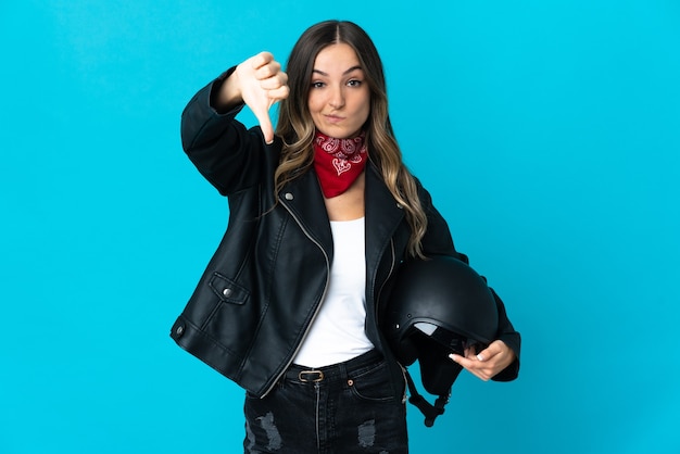 Romanian woman holding a motorcycle helmet isolated on blue background showing thumb down with negative expression