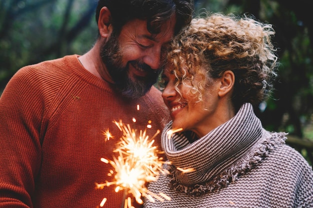 Photo romantic adult couple enjoy and love together with fire sparkler light in the forest green trees background man and woman with tenderness and relationship celebrate with firelight and smile