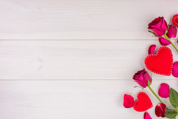 Romantic background with roses and hearts on a white wooden table. Top view, copy space.