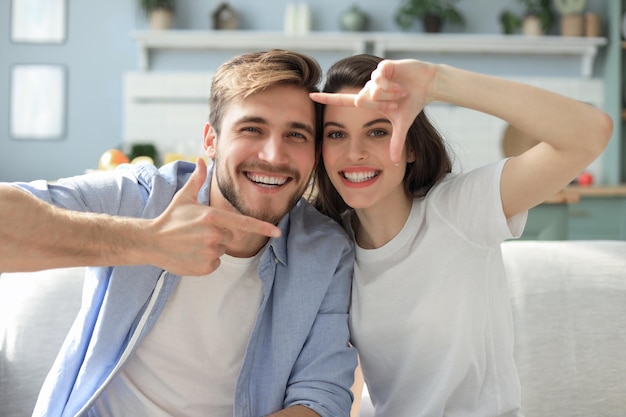 Bella coppia sorridente romantica che fa selfie per divertimento, a casa seduto sul divano.