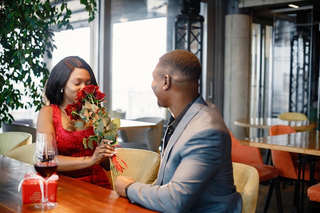 Foto romantica coppia nera seduta al ristorante che indossa abiti eleganti