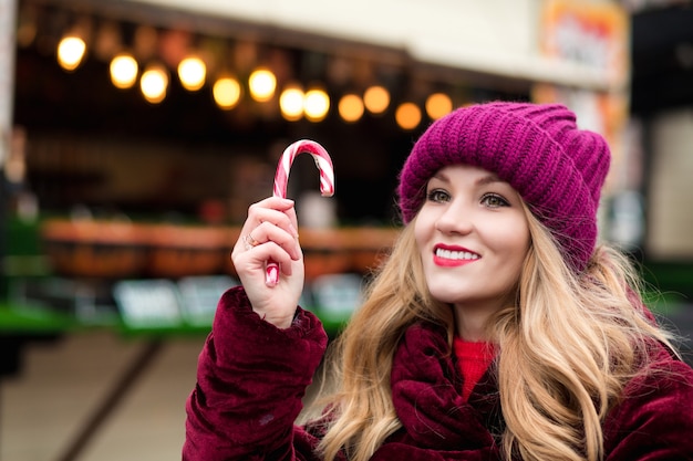 Romantic blonde woman posing with Christmas candy cane at the street