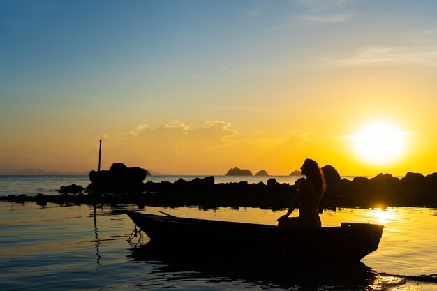 Romantic boat trip with a girl at sunset. The girl is sitting in a wooden boat on the ocean.