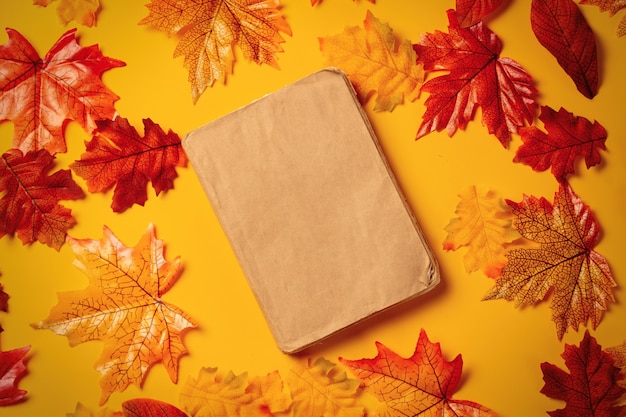 Libro romantico con foglie d'autunno su sfondo giallo. vista dall'alto